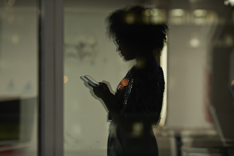 Reflection of young businesswoman checking smartphone in the office at night