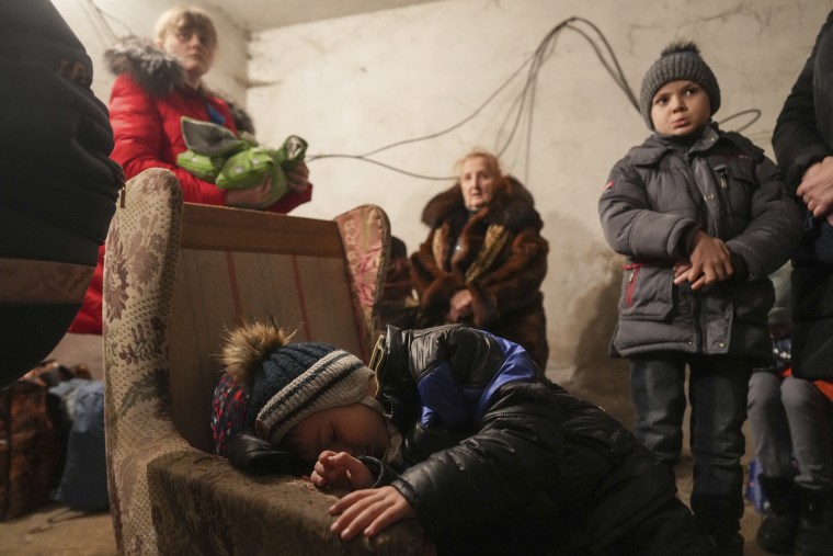 A child sleeps in an armchair as other stands around in a shelter during Russian shelling, in Mariupol, Ukraine.