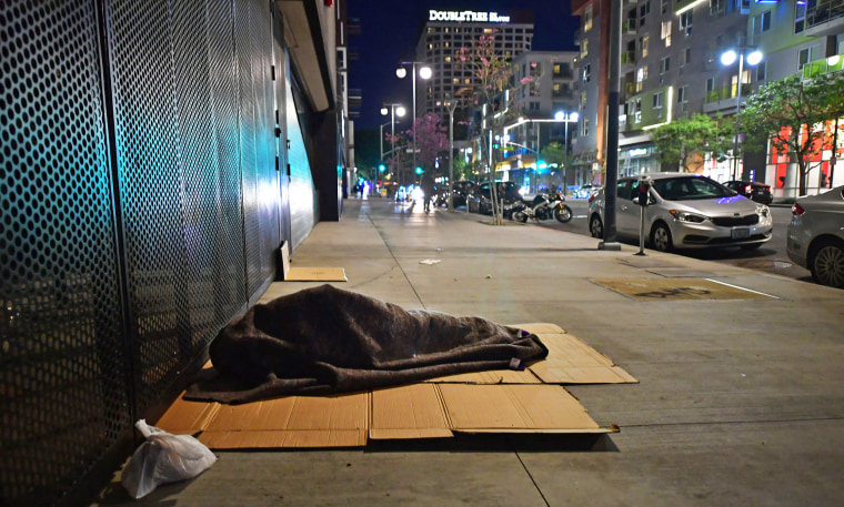 A homeless person sleeps on the sidewalk in Los Angeles