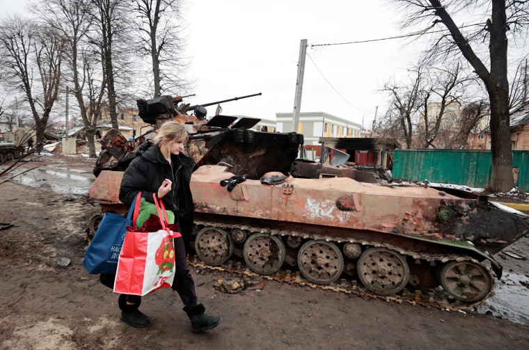 Image: A woman walks past a destroyed military vehicle in Bucha
