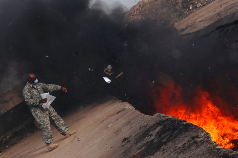 Image: An equipment manager tosses unserviceable uniform items into a burn pit in Iraq on March 10, 2008.