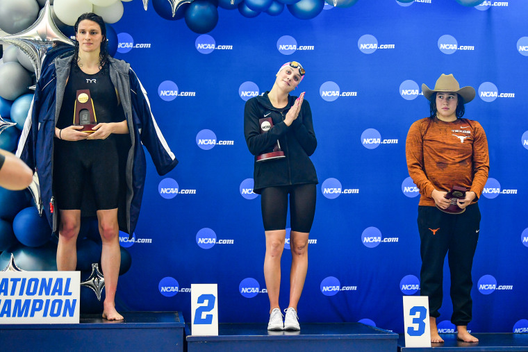 University of Pennsylvania swimmer Lia Thomas accepts the winning trophy for the 500 Freestyle finals as second place finisher Emma Weyant and third place finisher Erica Sullivan watch during the NCAA Swimming and Diving Championships on March 17, 2022, in Atlanta.