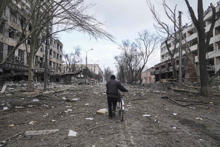 A man walks with a bicycle in a street devastated by shelling.