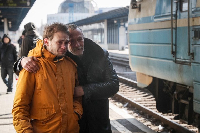 Men react as an evacuation train with their relatives departs to Lviv, at Kyiv central train station in Kyiv