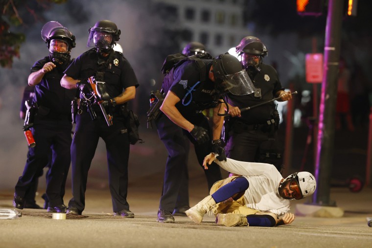 Denver Police Department officers clear a man who fell to the street after they used tear gas and rubber bullets to disperse a protest outside the State Capitol over the death of George Floyd, in Denver, on May 28, 2020.