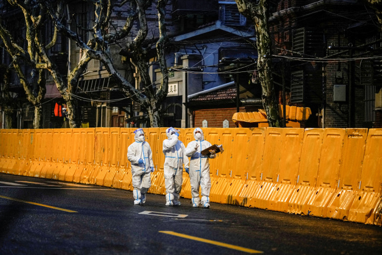 Image: Medical staff in personal protective equipment walk in front of barriers of an area under lockdown in Shanghai, China on March 25, 2022.