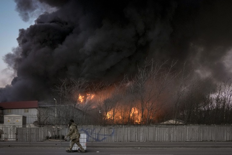 Soldados ucranianos que trasladan un contenedor pasan por delante de un incendio en un almacén tras un bombardeo, a las afueras de Kiev, Ucrania, el 17 de marzo de 2022.