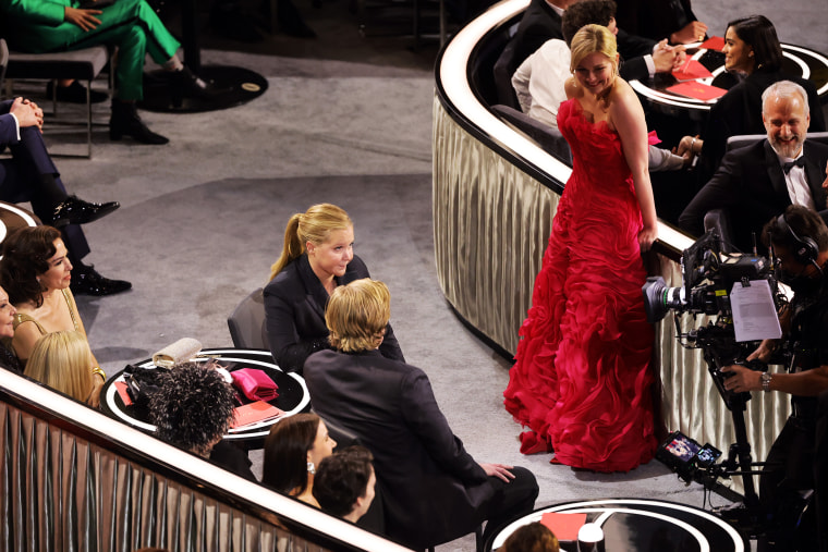 Amy Schumer sits next to Jesse Plemons on-camera as Kirsten Dunst looks on, laughing.