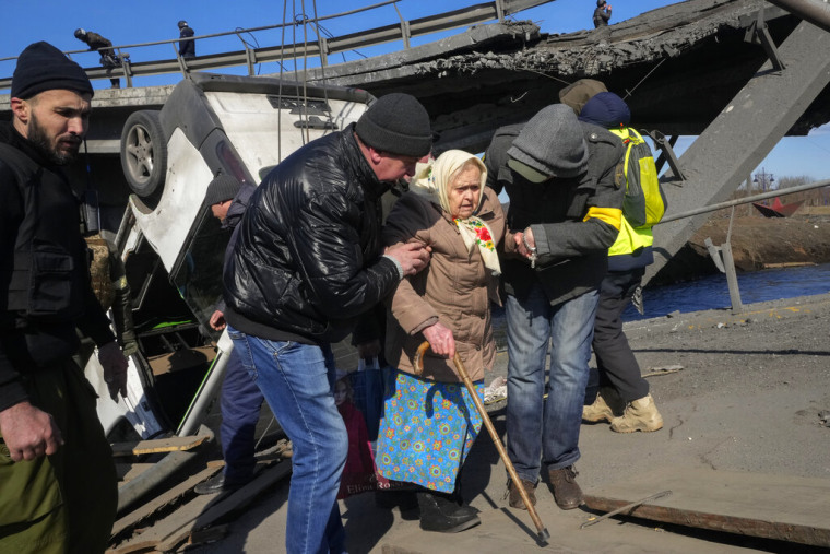 Voluntarios pasan por un camino improvisado debajo de un puente destruido mientras evacúan a una anciana residente en Irpin, al noroeste de Kiev, el viernes 11 de marzo de 2022.