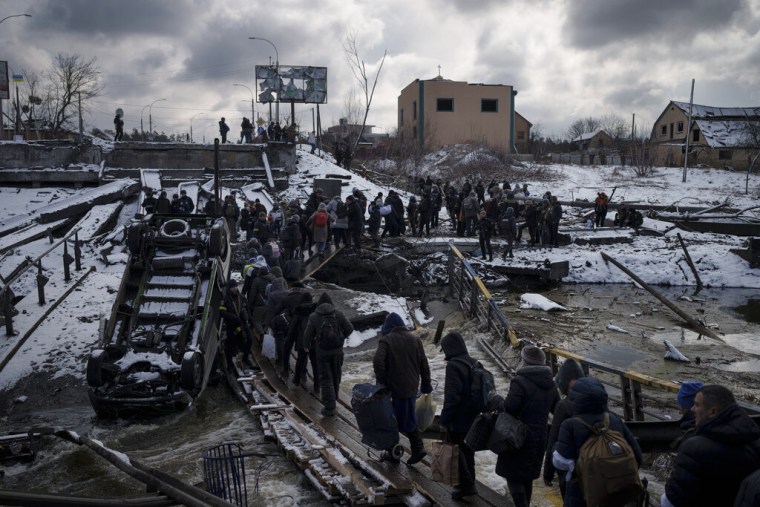 Ucranianos cruzan un camino improvisado bajo un puente destruido mientras huyen de Irpin, en las afueras de Kyiv, Ucrania, el martes 8 de marzo de 2022.