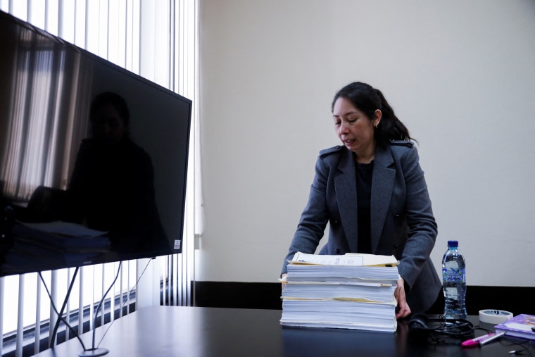 Una mujer latina con saco gris apila muchos papeles en sus oficinas de jueza en Guatemala.