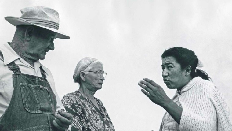 Una mujer latina gesticula mientras habla con dos granjeros
