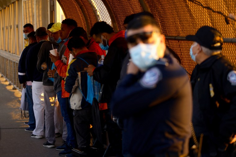 Migrantes solicitantes de asilo, bajo el programa de Protocolos de Protección al Migrante (MPP), esperan en el Puente Internacional Paso del Norte para asistir a una audiencia judicial de solicitud de asilo en Estados Unidos, Ciudad Juárez, México el 15 de marzo de 2022.