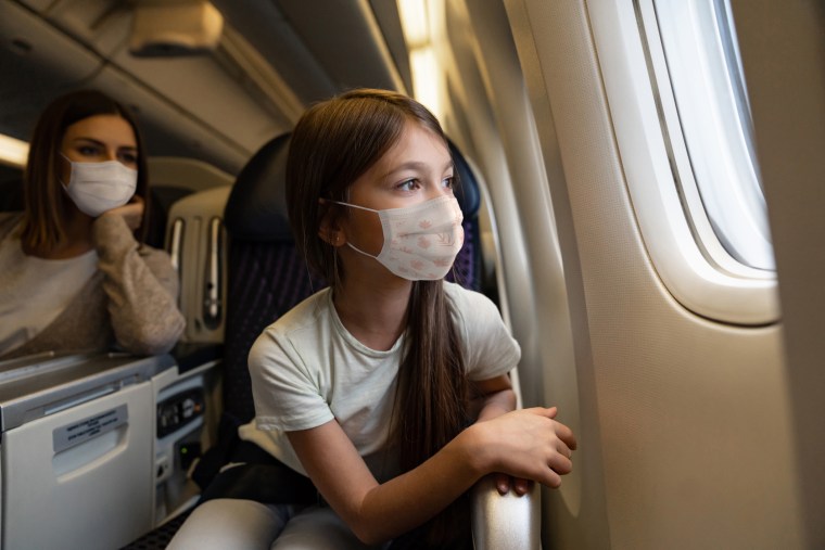 Happy girl traveling by plane wearing a facemask