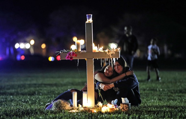 Image: Two people comfort each other as they sit to mourn at one of the seventeen crosses, after a candlelit vigil for victims of the shooting at Marjory Stoneman Douglas High School, in Parkland, Fla. , on February 15, 2018.