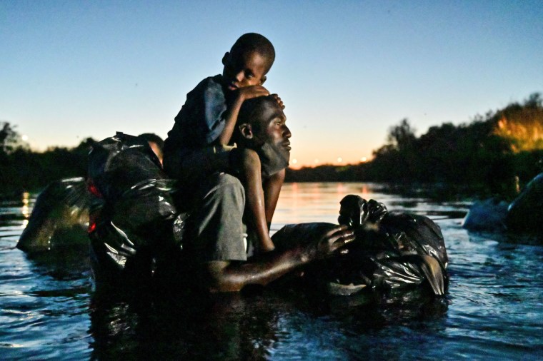 A man carries a child on his shoulders as Haitian migrants cross the Rio Grande river between Mexico and Del Rio, Texas, on Sept. 23, 2021.