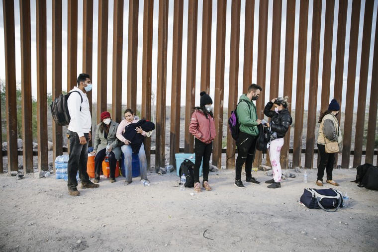 Asylum seekers from India, Cuba, and Colombia wait next to the U.S. border wall with Mexico, while being processed by U.S. border patrol in Yuma, Ariz., on Feb. 22, 2022.