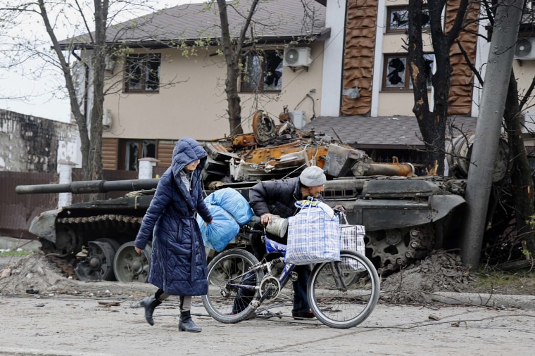 Local civilians walk past a tank destroyed during heavy fighting in an area controlled by Russian-backed separatist forces in Mariupol, Ukraine on Tuesday, April 19.