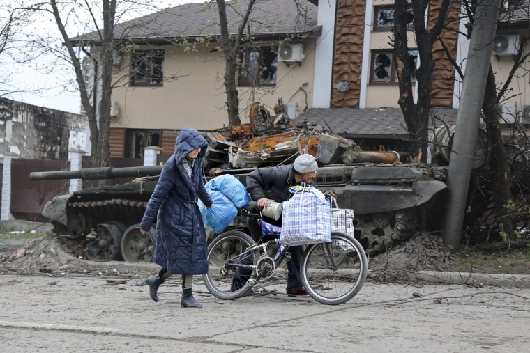 Civilians walk past a destroyed tank