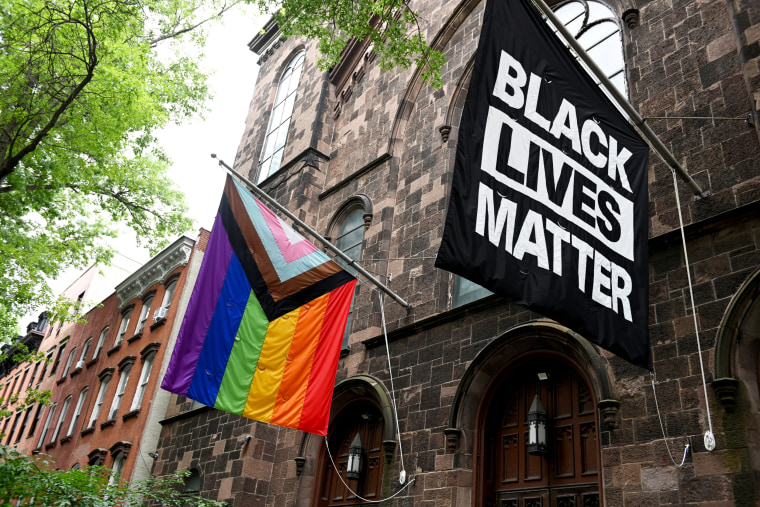 A progress pride flag and a Black Lives Matter flag are displayed outside a church