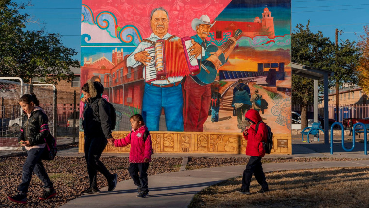 Habitantes latinos de El Paso caminan frente a un mural con motivos musicales, migratorios y de la comunidad hispana