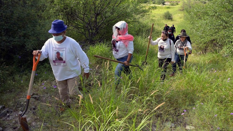 Un grupo de mujeres con picos y palas camina por un terreno boscoso. Son las Madres Buscadoras de Sonora, que excavan con la esperanza de encontrar restos de sus seres queridos
