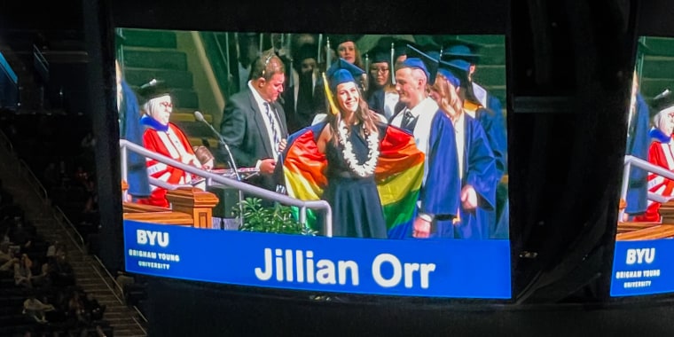 Brigham Young University graduate reveals a rainbow flag under her graduation cape while walking across the commencement stage Friday.
