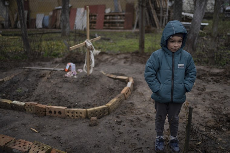 In the courtyard of their house, Vlad Tanyuk, 6, stands near the grave of his mother Maryna Tanyuk.