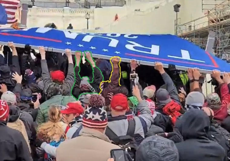 Defendant Marshall Neefe's right hand is visible, in yellow, as he and others pushed a “TRUMP” sign into a line of Metropolitan Police Department officers on Jan. 6, 2021, at the Capitol.