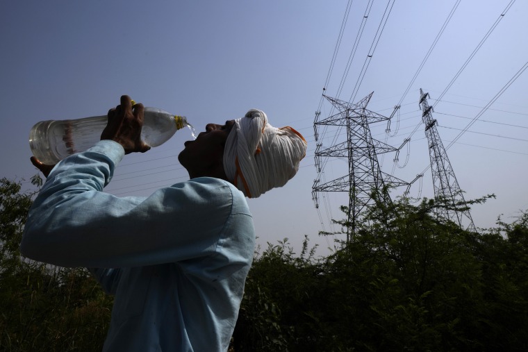 A worker quenches his thirst next to power lines as a heatwave continues to lash New Delhi on Monday.