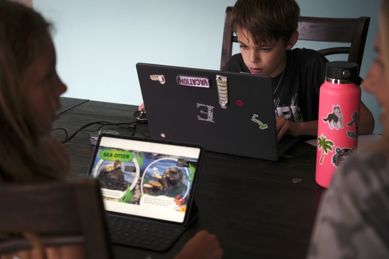 Kim Hough watches as her 12-year-old son, Ethan, and her 9-year-old daughter, Emelia, browse book selections on the Epic app at their home in Melbourne, Fla., on May 6.