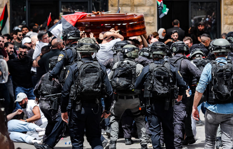 Image: Security forces and clash with mourners carrying a casket and Palestinian flags.