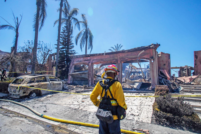 A firefighter stands outside one of the homes destroyed by the Coastal Fire