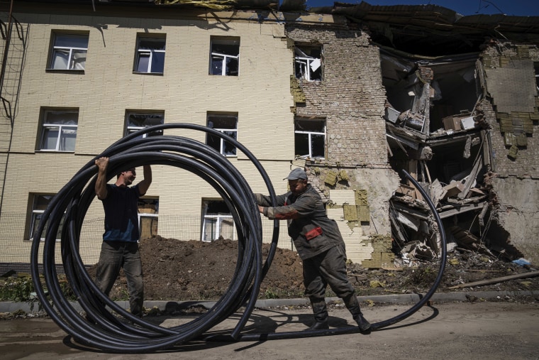 Municipal workers prepare a new tube to restore water supply in front of the building damaged by a Russian attack in Bahmut, Ukraine, on May 12, 2022. 