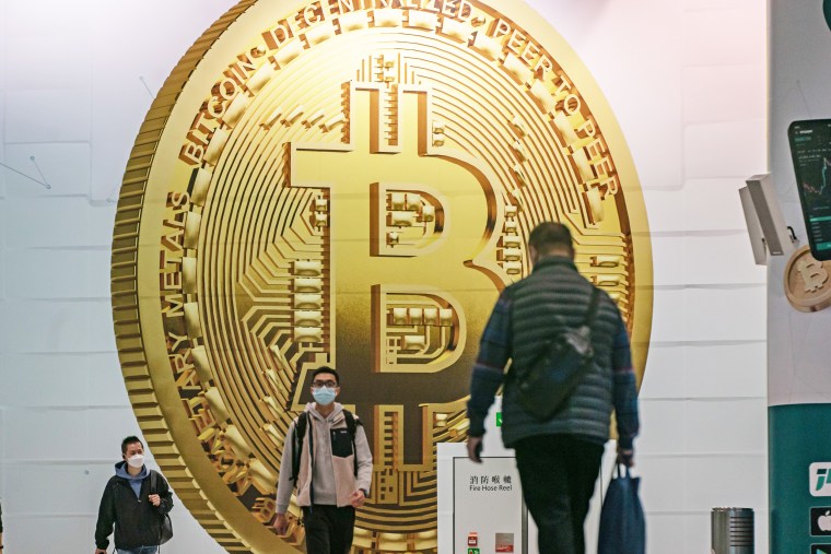 Pedestrians walk past an advertisement displaying a Bitcoin