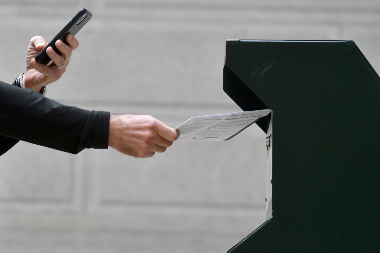 A man photographs himself depositing his ballot in an official ballot drop box while a long line of voters queue outside of Philadelphia City Hall at the satellite polling station in Philadelphia, on Oct. 27, 2020.
