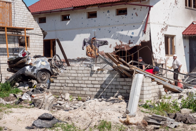 Sergey Ous, at right, stands outside his heavily damaged home in the village of Malaya Rohan, near Kharkiv.