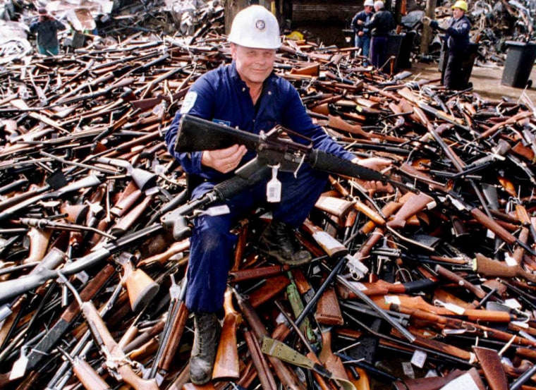 Seated on a pile of weapons, security firm project supervisor Norm Legg holds up an Armalite rifle, similar to the one used in the Port Arthur massacre, Melbourne, Victoria, Australia, on Sept. 8, 1996.