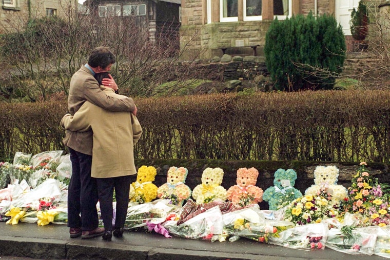A couple comforts each other as they view floral tributes to mark the death of children in a shooting tragedy in Dunblane, Scotland, on March 17, 1996.