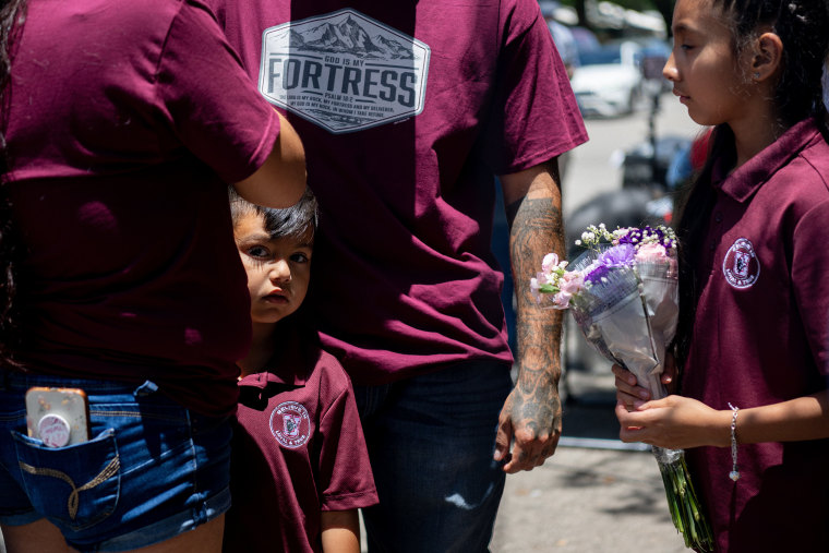Image.  A family waits to lay flowers at Robbie Elementary School on May 25, 2022 in Uvalde, Texas.