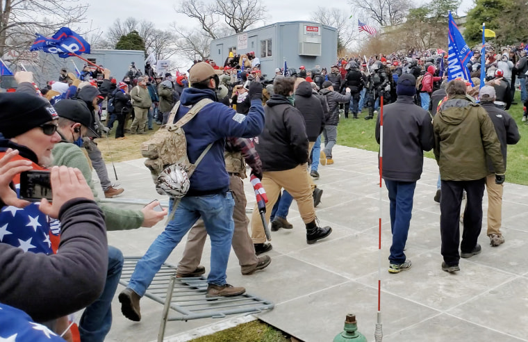 Image: Derek Kinnison, wearing a blue sweatshirt, steps on a police barrier as he approaches the  Capitol on Jan. 6, 2021.