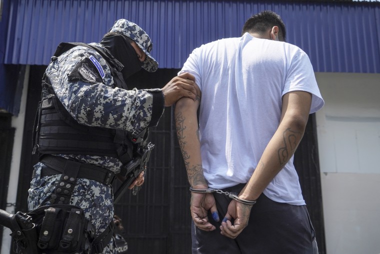 A hooded police officer escorts a suspected gang member