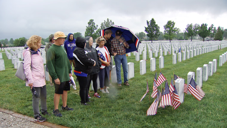 Dave Wirtz, in green, Sandy Wirtz , in an American flag vest, and Stephen Holley, in a blackshirt, pay respects at Scotty Wirtz’s grave.