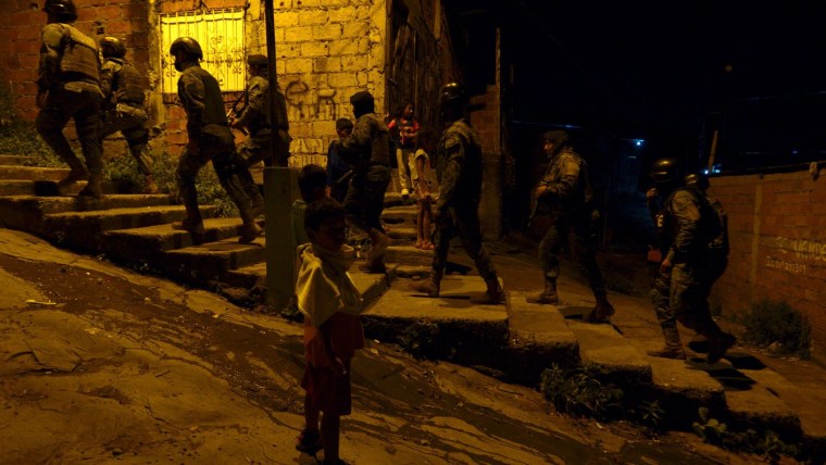 Soldados y policías suben una escalera frente como parte de su patrullaje por Guayas, Ecuador. Niños residentes de la zona empobrecida los miran.