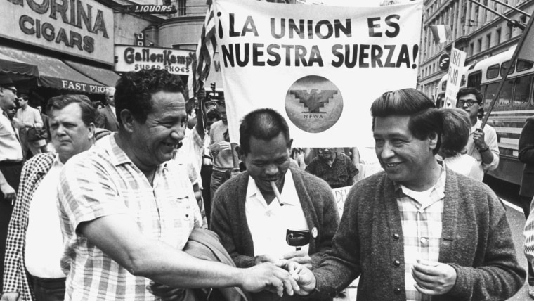 Tres hombres marchan durante una jornada de protesta en 1966 frente a un letrero que dice "La unión es nuestra fuerza".
