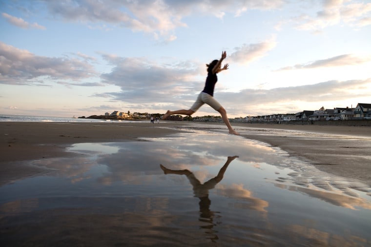 Woman leaping over puddle on beach