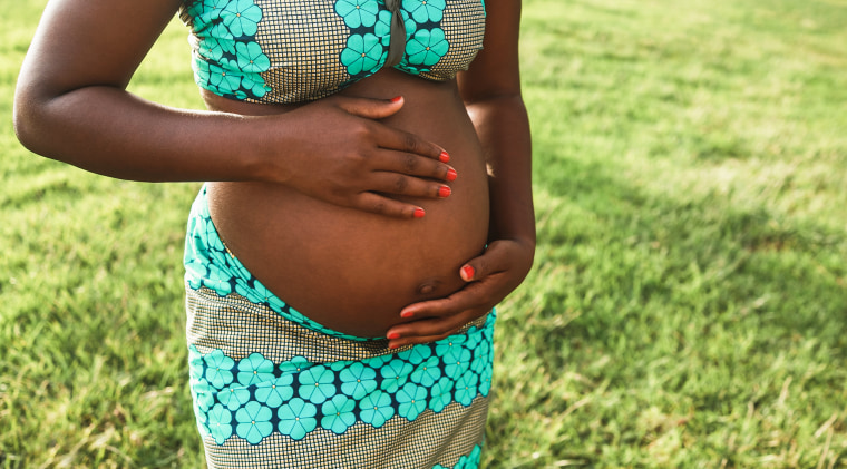 Young african pregnant woman having tender moment touching her belly outdoor - Focus on top hand