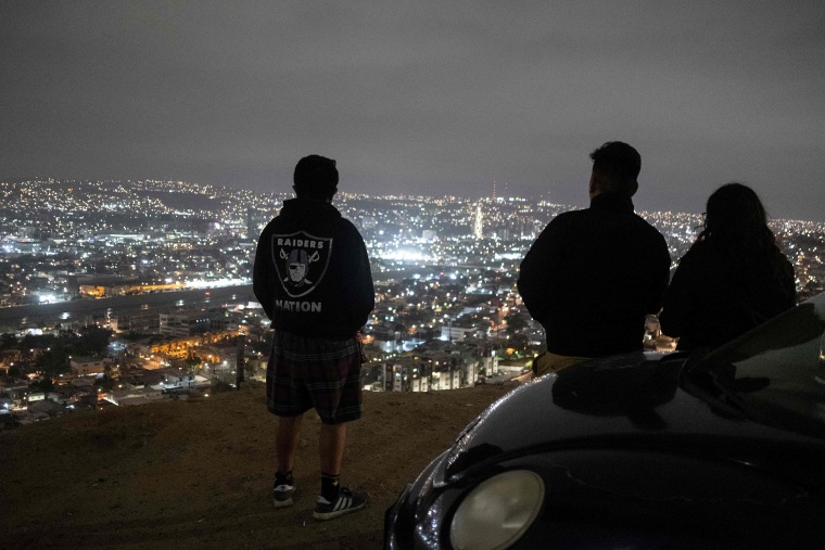 Image: A migrant from Guatemala, left, stands at a viewpoint with friends in Tijuana, Mexico on May 19, 2021, on his last day in the city before crossing to the United States to head to Los Angeles for his asylum process.