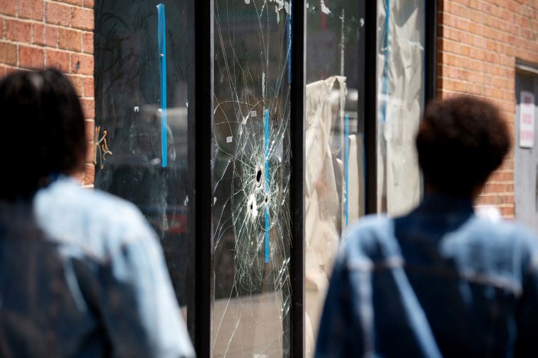 Pedestrians walk past bullet holes in the window of a store front on South Street in Philadelphia, Penn. on Sunday.