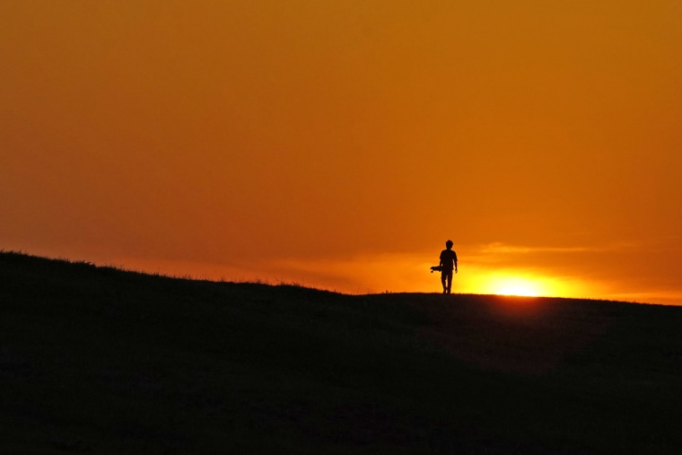 A skateboarder walks through a park at sunset Wednesday in San Antonio as temperatures in southern Texas continue to top the 100 degree mark. 